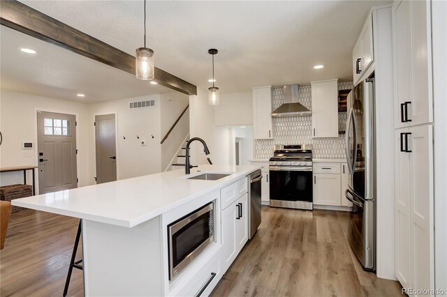 kitchen with visible vents, backsplash, appliances with stainless steel finishes, a sink, and wall chimney exhaust hood