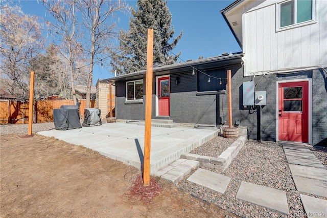 rear view of property featuring entry steps, fence, a patio, and brick siding