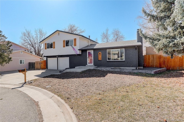 tri-level home featuring driveway, a chimney, an attached garage, fence, and brick siding