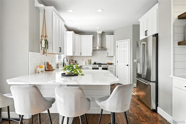 6039 Quay Ct, Arvada, CO 80003 - kitchen with appliances with stainless steel finishes, wall chimney exhaust hood, a peninsula, dark wood-style flooring, and light countertops