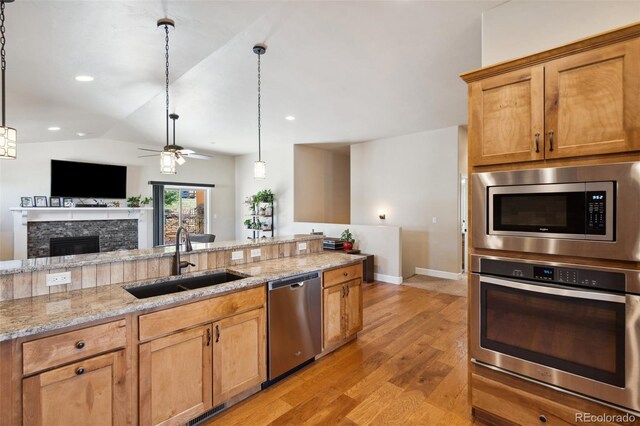 12441 Woodruff Dr, Colorado Springs, CO 80921 - kitchen featuring appliances with stainless steel finishes, a sink, light wood-style flooring, ceiling fan, and a stone fireplace