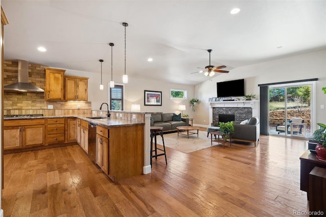 12441 Woodruff Dr, Colorado Springs, CO 80921 - kitchen featuring wall chimney exhaust hood, a sink, a kitchen breakfast bar, a fireplace, and light wood-style floors