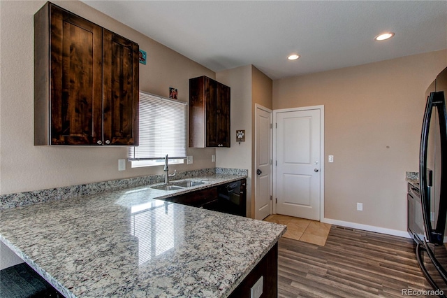 kitchen featuring light stone counters, black appliances, a peninsula, and dark brown cabinets