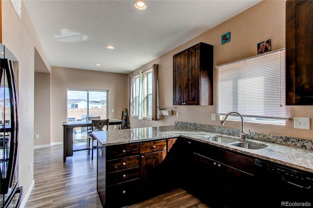 kitchen with a peninsula, a sink, light stone countertops, dark wood-style floors, and black appliances