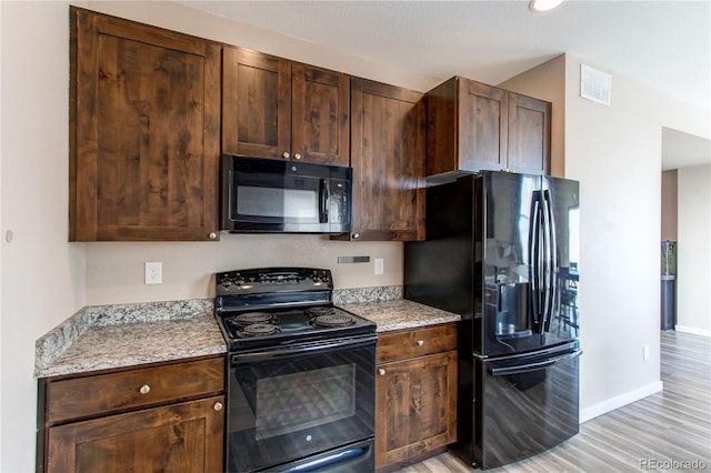 kitchen featuring light wood finished floors, visible vents, baseboards, light stone counters, and black appliances