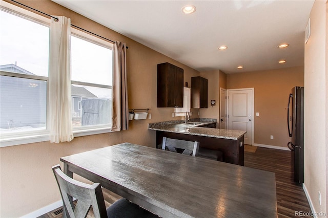 kitchen with dark brown cabinetry, dark wood-style flooring, freestanding refrigerator, a peninsula, and a sink