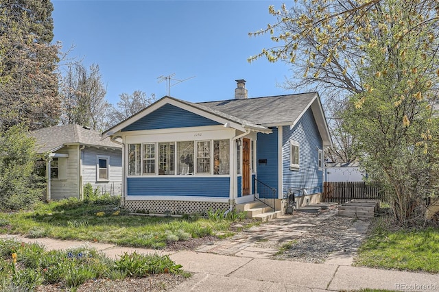 bungalow-style home featuring fence, a chimney, a shingled roof, and entry steps