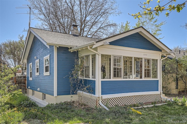view of side of home with fence, a chimney, a sunroom, and roof with shingles