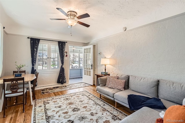 living room with a ceiling fan, french doors, crown molding, wood finished floors, and a textured wall