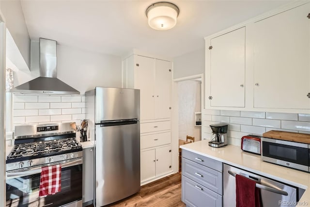 kitchen featuring light countertops, tasteful backsplash, wall chimney range hood, and stainless steel appliances