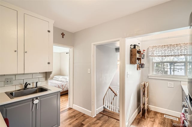kitchen featuring gray cabinets, visible vents, light wood-type flooring, a sink, and baseboards