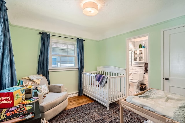 bedroom featuring crown molding, a crib, wood finished floors, and a baseboard radiator