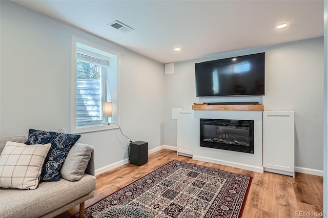 living area with baseboards, visible vents, a glass covered fireplace, and light wood-type flooring