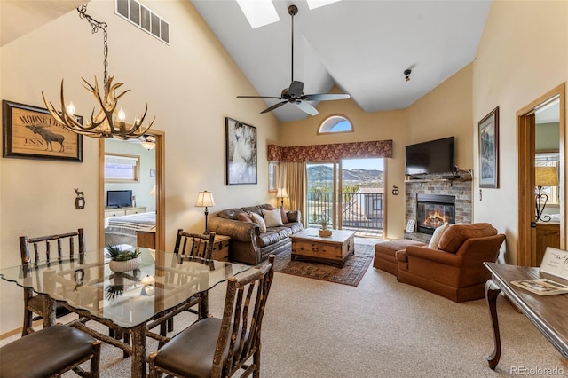 carpeted dining space with a skylight, a glass covered fireplace, high vaulted ceiling, a chandelier, and ceiling fan