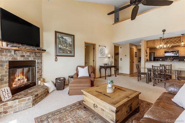 carpeted living room with a chandelier, a ceiling fan, a brick fireplace, and a towering ceiling