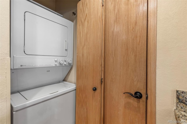 clothes washing area featuring stacked washer and clothes dryer and a textured wall