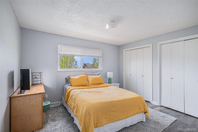 bedroom with two closets, a textured ceiling, and baseboards