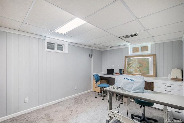 carpeted home office with wood walls, baseboards, visible vents, and a drop ceiling