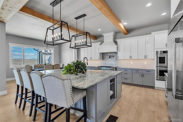 7668 Buckskin Ranch Vw, Peyton, CO 80831 - kitchen with custom exhaust hood, tasteful backsplash, an inviting chandelier, beamed ceiling, and appliances with stainless steel finishes