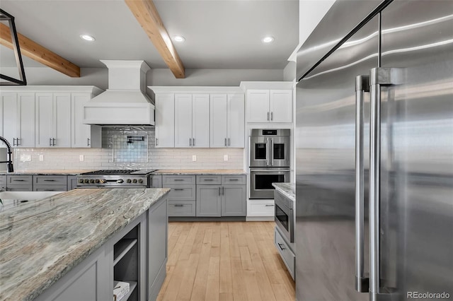 7668 Buckskin Ranch Vw, Peyton, CO 80831 - kitchen featuring premium appliances, light wood-style floors, beamed ceiling, custom range hood, and backsplash