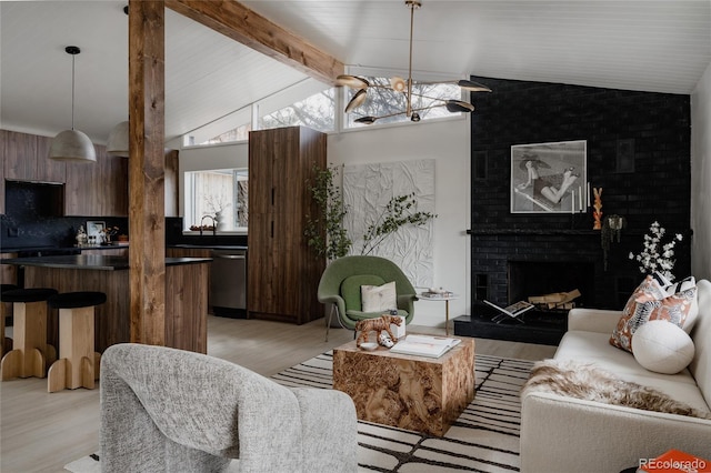 living room with lofted ceiling with beams, a brick fireplace, a notable chandelier, and light wood-type flooring