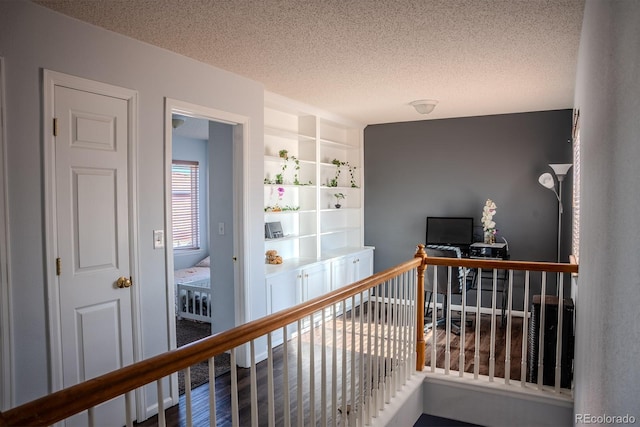 hall with built in shelves, wood-type flooring, and a textured ceiling