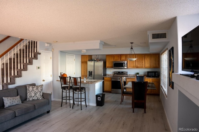 interior space with pendant lighting, a breakfast bar area, light hardwood / wood-style flooring, appliances with stainless steel finishes, and a textured ceiling