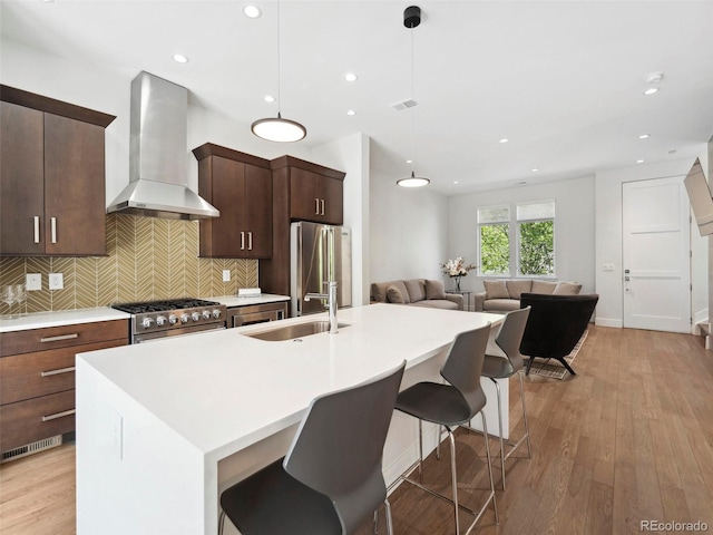 kitchen featuring pendant lighting, a center island with sink, high end appliances, and wall chimney range hood