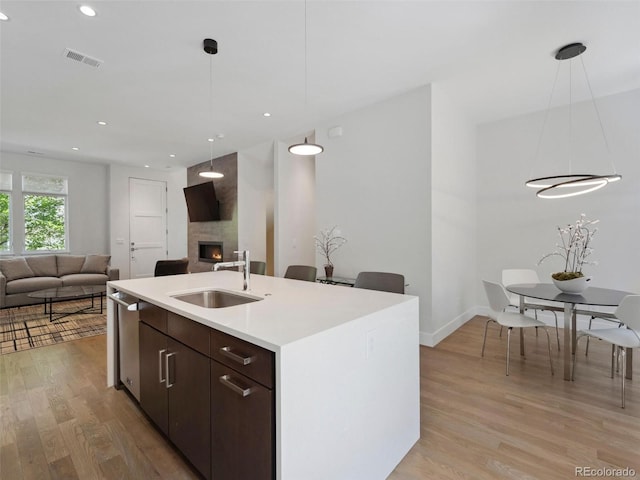 kitchen featuring dark brown cabinets, a large fireplace, sink, light hardwood / wood-style floors, and an island with sink