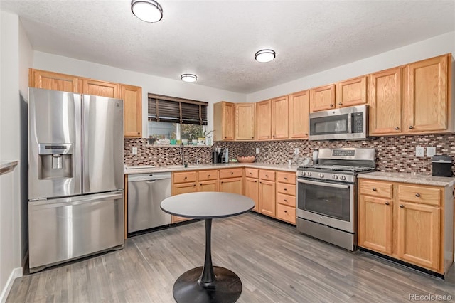 1371 W 133rd Way, Denver, CO 80234 - kitchen with stainless steel appliances, light brown cabinetry, light wood-type flooring, light countertops, and a textured ceiling
