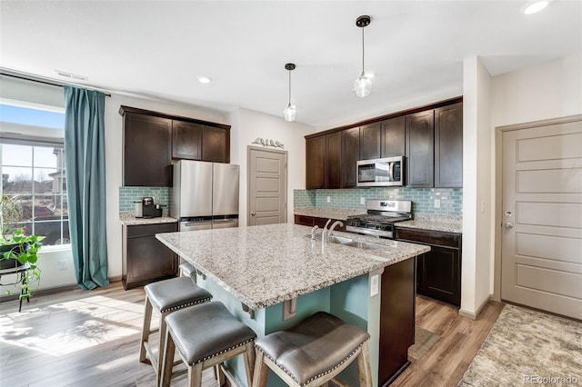 kitchen with light stone countertops, a sink, dark brown cabinetry, appliances with stainless steel finishes, and light wood-type flooring