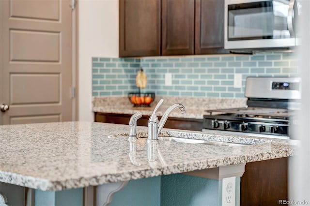 kitchen featuring tasteful backsplash, dark brown cabinets, appliances with stainless steel finishes, and light stone countertops