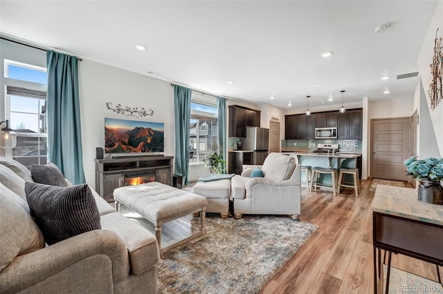 living room featuring visible vents, recessed lighting, a warm lit fireplace, and light wood-type flooring