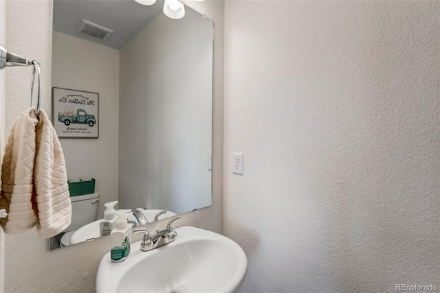 half bathroom with visible vents, a textured wall, and a sink