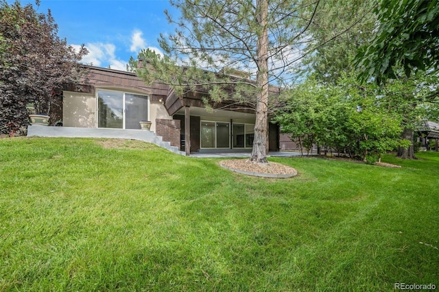 rear view of house featuring a lawn and stucco siding