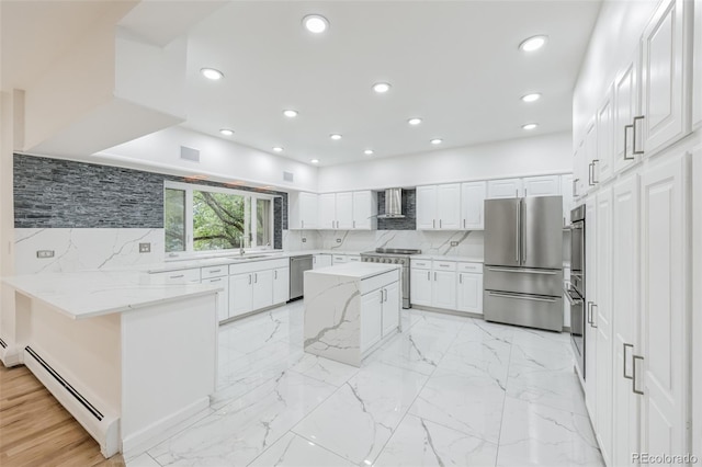 kitchen with a baseboard radiator, wall chimney exhaust hood, decorative backsplash, stainless steel appliances, and white cabinets