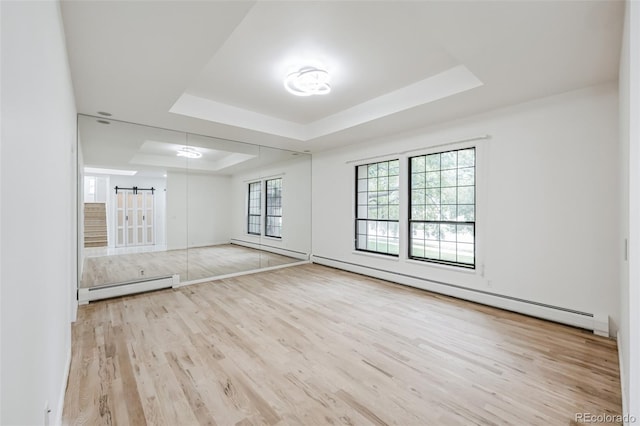 empty room featuring a baseboard heating unit, a tray ceiling, and light wood-type flooring