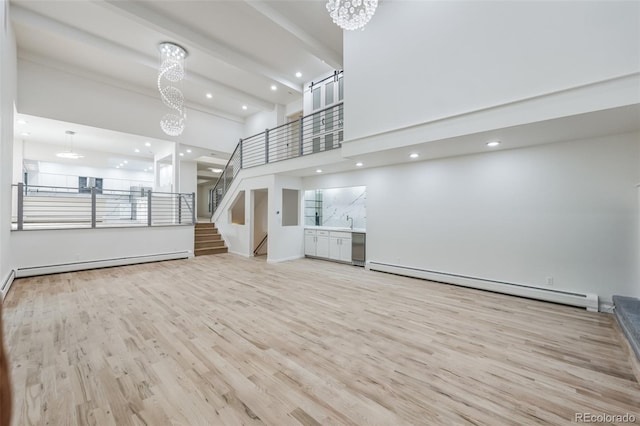 unfurnished living room featuring baseboard heating, light hardwood / wood-style flooring, a chandelier, a towering ceiling, and beamed ceiling