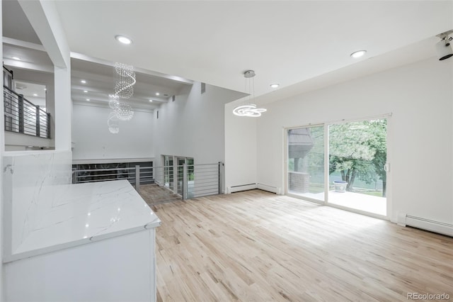 kitchen with light hardwood / wood-style floors, light stone counters, baseboard heating, and decorative light fixtures