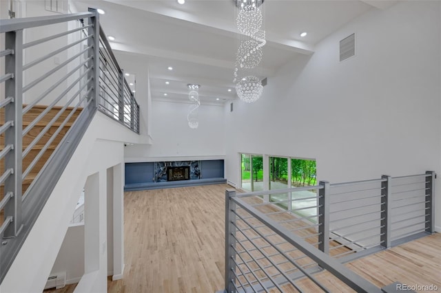 unfurnished living room with wood finished floors, an inviting chandelier, a high ceiling, baseboard heating, and beam ceiling