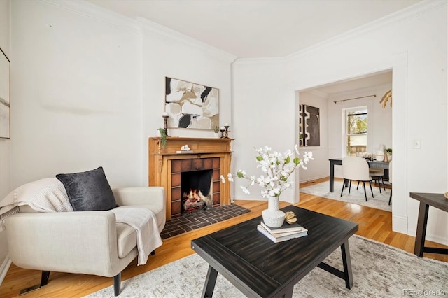 living room with a tiled fireplace, light wood-style flooring, baseboards, and ornamental molding