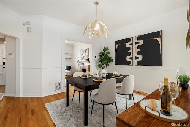dining area featuring visible vents, light wood-style floors, a notable chandelier, and ornamental molding