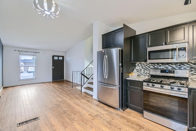 kitchen featuring light wood-type flooring, appliances with stainless steel finishes, tasteful backsplash, and light stone countertops