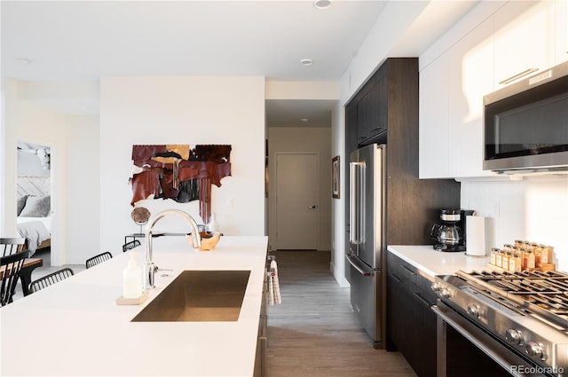 kitchen with appliances with stainless steel finishes, sink, white cabinetry, and light hardwood / wood-style flooring