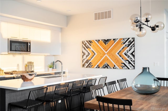 kitchen featuring an inviting chandelier, white cabinetry, kitchen peninsula, a breakfast bar, and sink