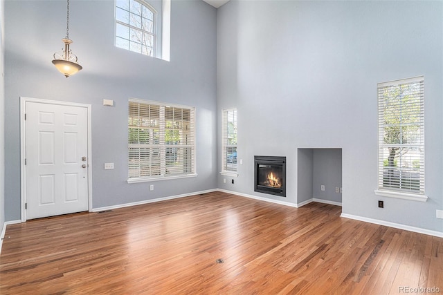 unfurnished living room featuring a high ceiling, wood finished floors, a glass covered fireplace, and baseboards