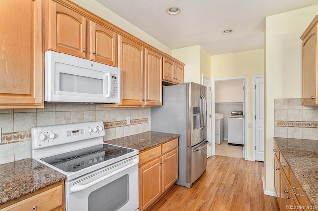 kitchen featuring white appliances, washing machine and dryer, light wood-type flooring, dark stone counters, and recessed lighting