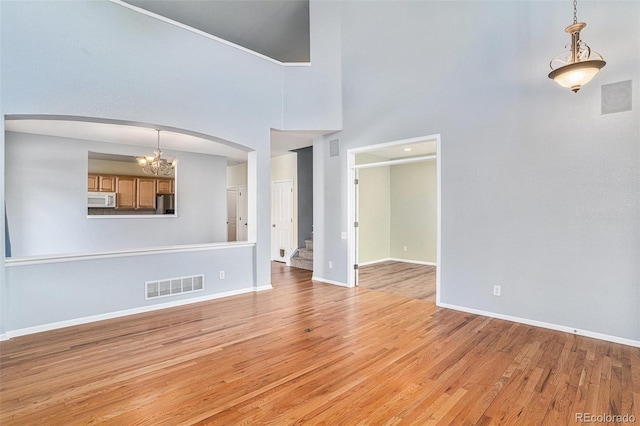 unfurnished living room with a chandelier, arched walkways, baseboards, light wood-style flooring, and a towering ceiling