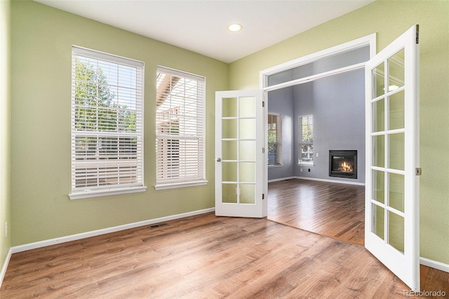 unfurnished living room featuring french doors, wood finished floors, baseboards, a glass covered fireplace, and recessed lighting