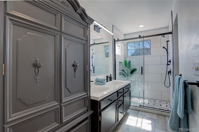 full bath with wood finished floors, double vanity, a sink, a shower stall, and tile walls